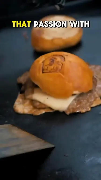 A burger on a griddle at a market stall, with a yellow caption across the top.